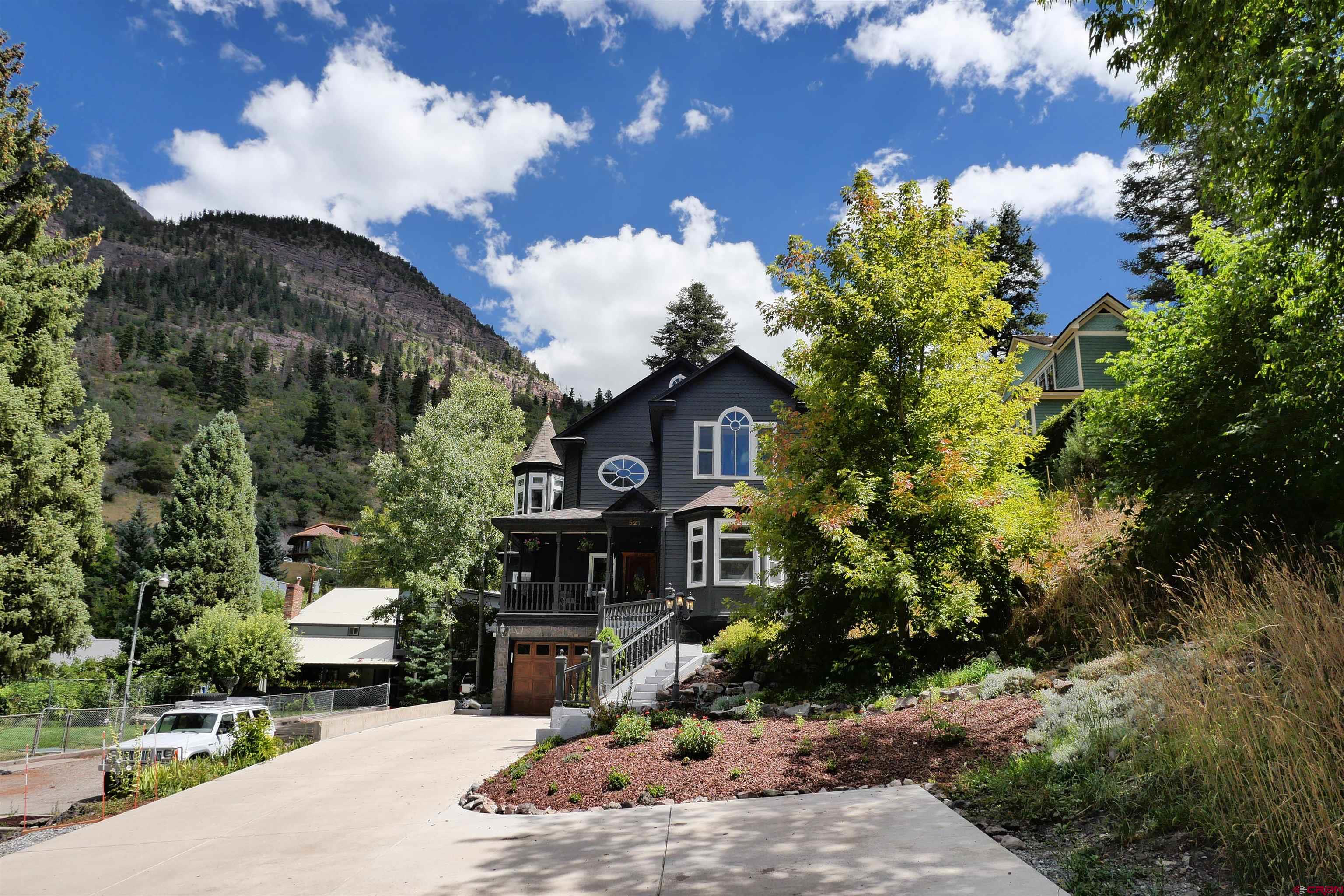 Discover this meticulously crafted home in the Heart of Ouray, strategically positioned to embrace the charm of the Gem of the Rockies. Nestled at the base of the beloved Vinegar Hill, Ouray's iconic sledding spot, this residence offers sweeping vistas of the valley, including the Rock of Ages and Twin Peaks.  Living here provides direct access to popular hiking destinations like Chief Ouray Mine, Cascade Falls, Box Canyon, Perimeter Trail, and the Ice Park. Ouray School, essential shops, restaurants, and the Hot Springs are all within easy walking distance.  What sets this location apart is its tranquility and privacy. This residential enclave experiences minimal traffic and prohibits short-term rentals, ensuring a serene atmosphere without the hustle and bustle found in other parts of town.  The house itself is a masterpiece with exquisite interior and exterior finishes. Spacious rooms, elegant trim work, regal lighting fixtures, and oversized windows create warm and inviting spaces for gatherings with loved ones.  Approaching the main entrance, you'll ascend a grand stairway from the generous west-side parking area, passing manicured gardens and a charming brick sitting area. The soothing sound of flowing hot spring water, a testament to Ouray's allure, can be enjoyed year-round from the west-facing wrap-around front porch.  Inside, the front entrance welcomes you with an impressive winding stairway leading to the upper level and an open floorplan on the main level. To your right, a beautiful sitting room boasts a built-in fireplace and windows overlooking the Sledding Hill and Town. Moving towards the rear, a spacious dining room awaits your guests.  Adjacent is a sizable media-family room connected to a secluded mountain patio with a built-in barbecue, stone walls, and manicured gardens. The kitchen is a culinary haven, featuring marble counters, top-of-the-line appliances, a walk-in pantry, and ornate custom cabinetry.  The stairway to the upper level is a work of art itself, leading to a versatile space at the front of the home ideal for an office, library, or workout room. As you progress towards the back, you'll discover the impressive guest bathroom and two spacious bedrooms along the southern side.  At the rear of the home, a splendid primary suite boasts east-facing windows and a spacious, luxurious bath. The rounded cupola area within the bathroom provides a breathtaking view of the mountains.  The property offers a two-car oversized garage accessed from the alley on the east side and a small garage underneath the front area that can serve as a gear storage space for ATVs, golf carts, or a Jeep. It also houses the ultra-efficient natural gas in-floor heating system.  This meticulously maintained home in Southwest Colorado is suitable for year-round living, a seasonal escape, or weekend retreat. The sellers are generously offering it fully furnished, with just a few exceptions, simplifying your transition.  If you've ever dreamt of calling Ouray your home, don't miss the opportunity to make this regal residence in the Heart of Ouray your new legacy. Schedule a viewing today.