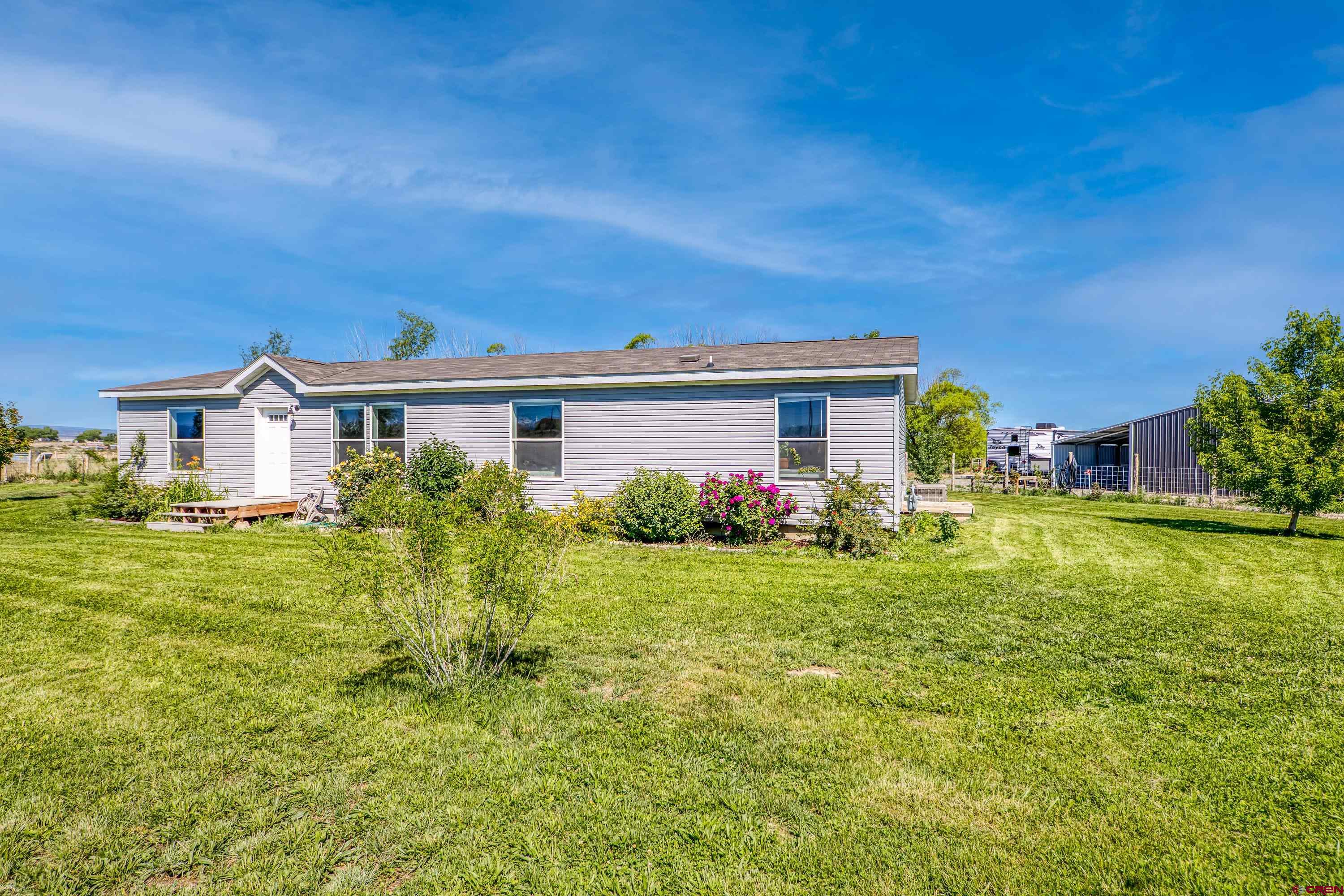 Welcome to Western Colorado! Come and see this charming and beautifully maintained, spacious 4-year-old, 3 Bed, 2 Bath manufactured home on 3.13 irrigated acres! You can also build an additional, single-family residence on the parcel with NO Size Restriction and NO HOA covenants! It is perfect for multi-generational living which is in high demand, or potential rental income. The open floorplan is spacious, light, bright and inviting and the colors are soothing. There is lovely crown molding throughout the home. The primary suite bathroom with large soaking tub and walk-in shower feels like a spa. This meticulous home looks new and is just waiting for game nights and cookouts! Enjoy cool summer mornings having coffee on the spacious deck, listening to the small pond. Wander through the lush lawn (with sprinkler system) and notice the beautiful plantings around the property and the striking Cimmaron/San Juan mountain views to the south, and the Grand Mesa to the NW. Outdoor recreation surrounds you here! The 20' x 30' garage/shop and attached carport provide plenty of storage for your toys, and RV parking has electricity in place. The yard is fenced and ready for your hobby farm, small orchard etc. and with a low $129 annual irrigation fee, there is so much potential for gardens, vineyard, greenhouse etc.! Just outside city limits for a country feel and lower taxes, but close to all Montrose amenities, riding trails, multiple golf courses, fishing, Black Canyon National Park, and the newly expanded airport. Telluride and Crested Butte are approx. 60-80 mins. away. Montrose is on the radar now as people have discovered our mild winter climate, with high mountains nearby for world class summer and winter sports! Properties with irrigation are being snapped up quickly so schedule your showing today! We live the Real Colorado Lifestyle here in Montrose!