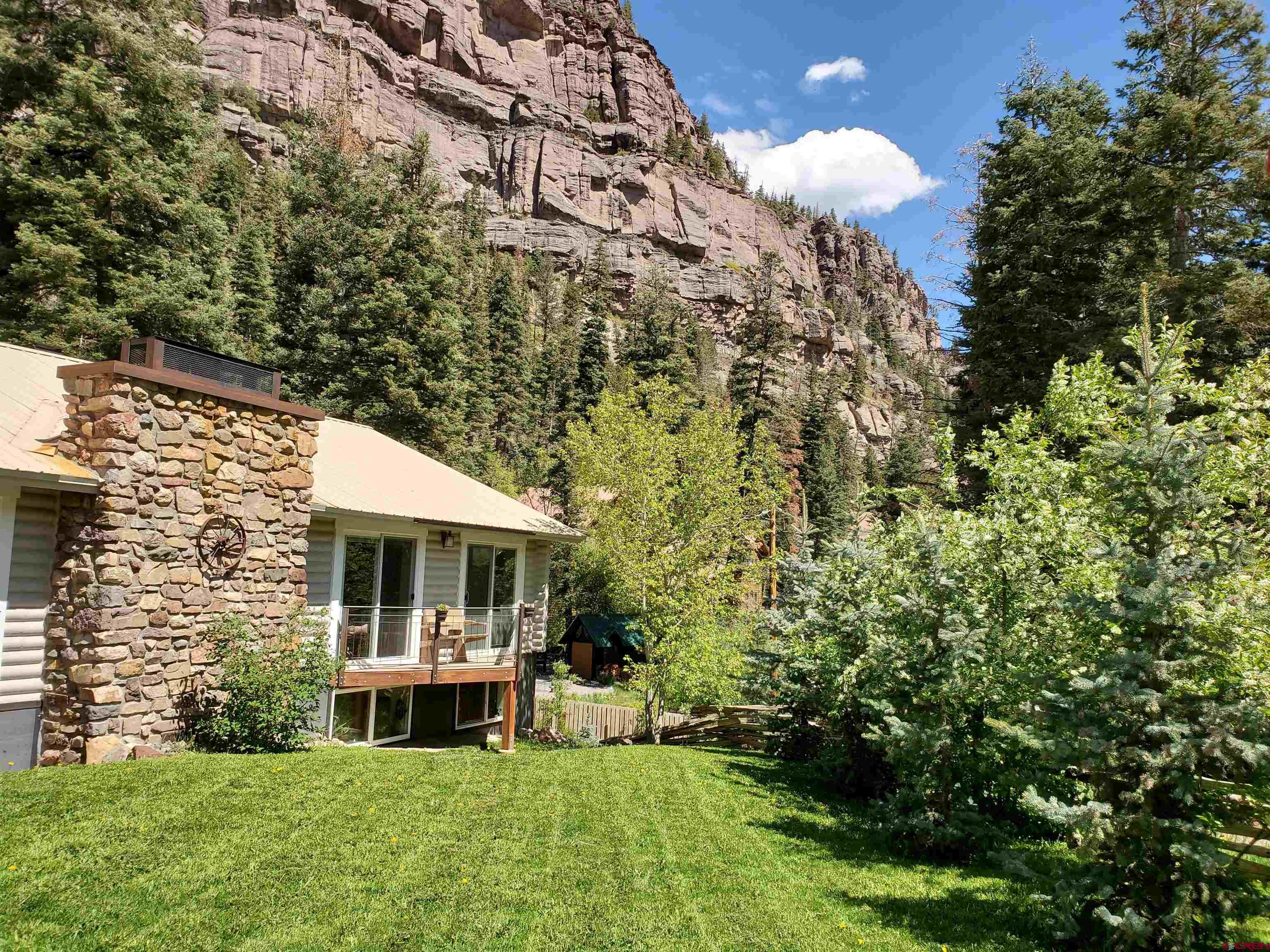 Nestled in the heart of Ouray on a large private lot with stunning views, this modern, warm, and cozy setting invites you to unwind and feel at home.  The open floor plan seamlessly integrates indoor and outdoor living, allowing natural light to flood the space, highlighting the rich textures and contemporary design.   Imagine sipping your morning coffee on the balcony, gazing out at breathtaking views or enjoying a quiet evening of serenity.   The fully equipped kitchen, adorned with sleek appliances and ample storage, is a culinary enthusiast's dream. A bonus 2nd kitchen on the lower level allows for an additional living quarter. Generous sized bedrooms suited for king sized furniture. A portion of the home is warmed by in floor radiant heated tile floors.  Detached oversized 2 car garage currently a wood shop with 220-amp service and a bear proof chicken coop or storage as needed. Additional log storage building and a partially fenced yard with a gate entranced drive.  Truly an inviting home.