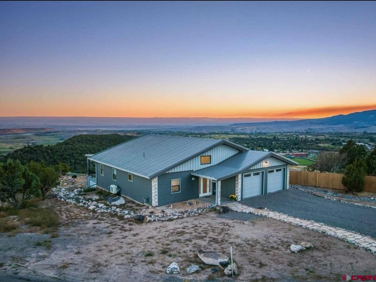 You will be amazed with the million dollar mountain and valley views from the low maintenance south facing 12’x50’ covered deck on the back of this well-built steel framed one level home.  Enjoy sun rises and sunsets and the entire valley floor and the breathtaking views of the West Elk Range, the Grand Mesa, Black Canyon, the Sneffles Range in the San Juans and Harts Basin Reservoir.   This immaculate 3 bedroom, 2 full bath, 1,984 SF steel frame home has a no maintenance metal exterior as well.  Your eyes will be drawn to the soaring ceilings in the foyer which leads to the beautiful open concept living area and on out to the deck to take in the amazing views!  The open kitchen has soft closed doors, built-in pantry, granite countertops throughout the home and a top end stainless steel appliance package.  The primary suite is large and luxurious with a nice walk-in closet, 5 piece ensuite with double sink vanity, soaker tub and separate shower and large walk-in closet.  The home has solid core doors, natural gas in-floor hot water heat, and mini split units throughout the home for cooling as well as heating. The closets have closet systems installed and there is lots of storage along with fantastic insulation throughout.  Enjoy your evenings or morning coffee on the deck which runs the entire length of the home to enjoy your sunrises and sunsets! Oversized attached 2 car heated garage has room for larger vehicles, PLUS you can park an RV with an electrical hookup on the exterior of the garage.