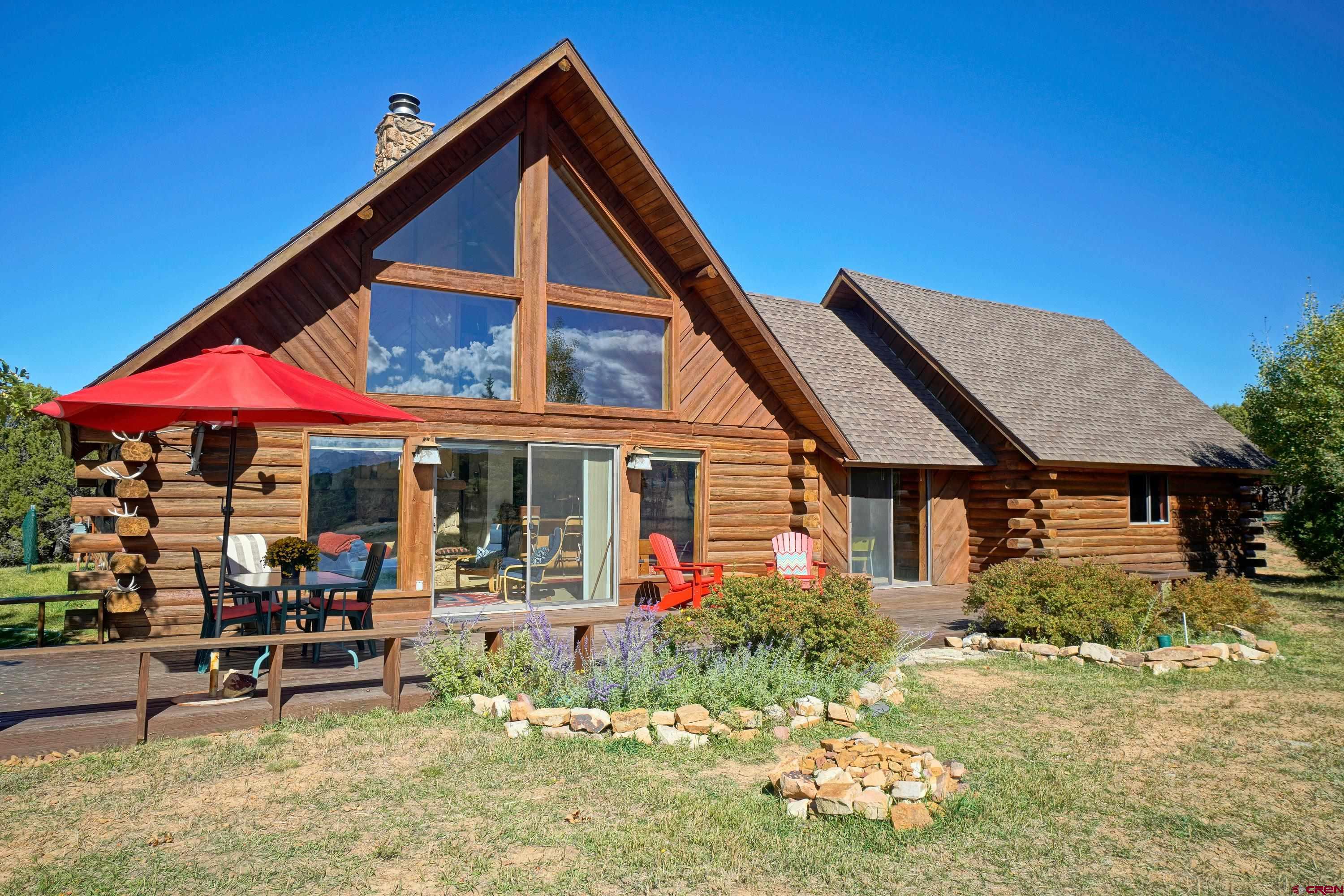 Welcome to your Colorado mountain retreat in the heart of Log Hill Village, one of Ouray County’s most sought-after communities. This custom-crafted log home sits on a sun-soaked knoll with sweeping views of the Sneffels Range and surrounding peaks. Here, you’ll experience the perfect balance of rustic character, modern comfort, and unbeatable access to all the San Juan lifestyle offers.  Step inside and be greeted by a dramatic great room with towering ceilings and floor-to-ceiling windows, designed to frame the mountain views and fill the space with natural light. A classic stone fireplace anchors the room, creating a warm gathering space that flows easily into a spacious dining area—perfect as is or ideal for conversion into an additional bedroom or entertainment space. The central kitchen is conveniently placed, while two comfortable guest bedrooms and a full bath round out the main level. Step onto the large south-facing deck to enjoy year-round sunshine, mountain air, and the sight of deer and wild turkeys wandering across your property.  Upstairs, the private primary suite offers its own full bath and a deck with panoramic views that stretch from the Grand Mesa to the Cimarrons to Horsefly Peak. Morning coffee or evening stargazing here will quickly become your favorite rituals. The oversized log-crafted garage with vaulted ceilings offers incredible flexibility—already beautiful for vehicles, but easily adaptable into additional living space or even a loft.  Life in Log Hill Village means endless opportunities for adventure and relaxation. From here, you’re just 5 minutes to Divide Ranch & Club Golf Course, 15 minutes to Ridgway, 30 minutes to Ouray, and less than an hour to skiing in Telluride. Take daily hikes on nearby trails like the scenic Escarpment Path, ride your e-bike on quiet country roads, or soak in natural hot springs after a day on the slopes. Festivals, fine dining, and friendly neighbors make this an unbeatable year-round or seasonal retreat.  Offered fully furnished and move-in ready, this special property is more than a home—it’s a mountain lifestyle waiting for you.