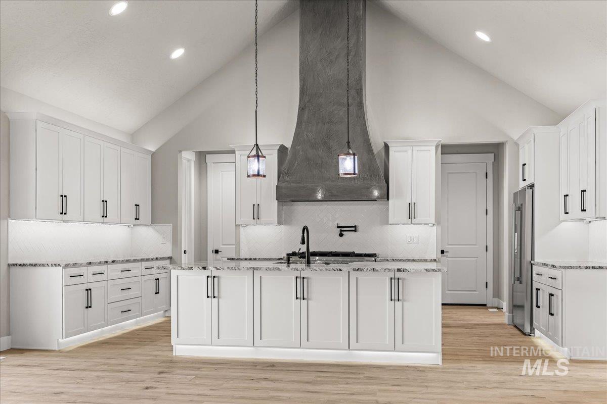 Kitchen featuring high vaulted ceiling, white cabinets, decorative light fixtures, light stone countertops, and light wood-style flooring