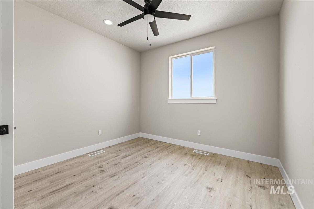 Empty room featuring a textured ceiling, light wood-style floors, and ceiling fan