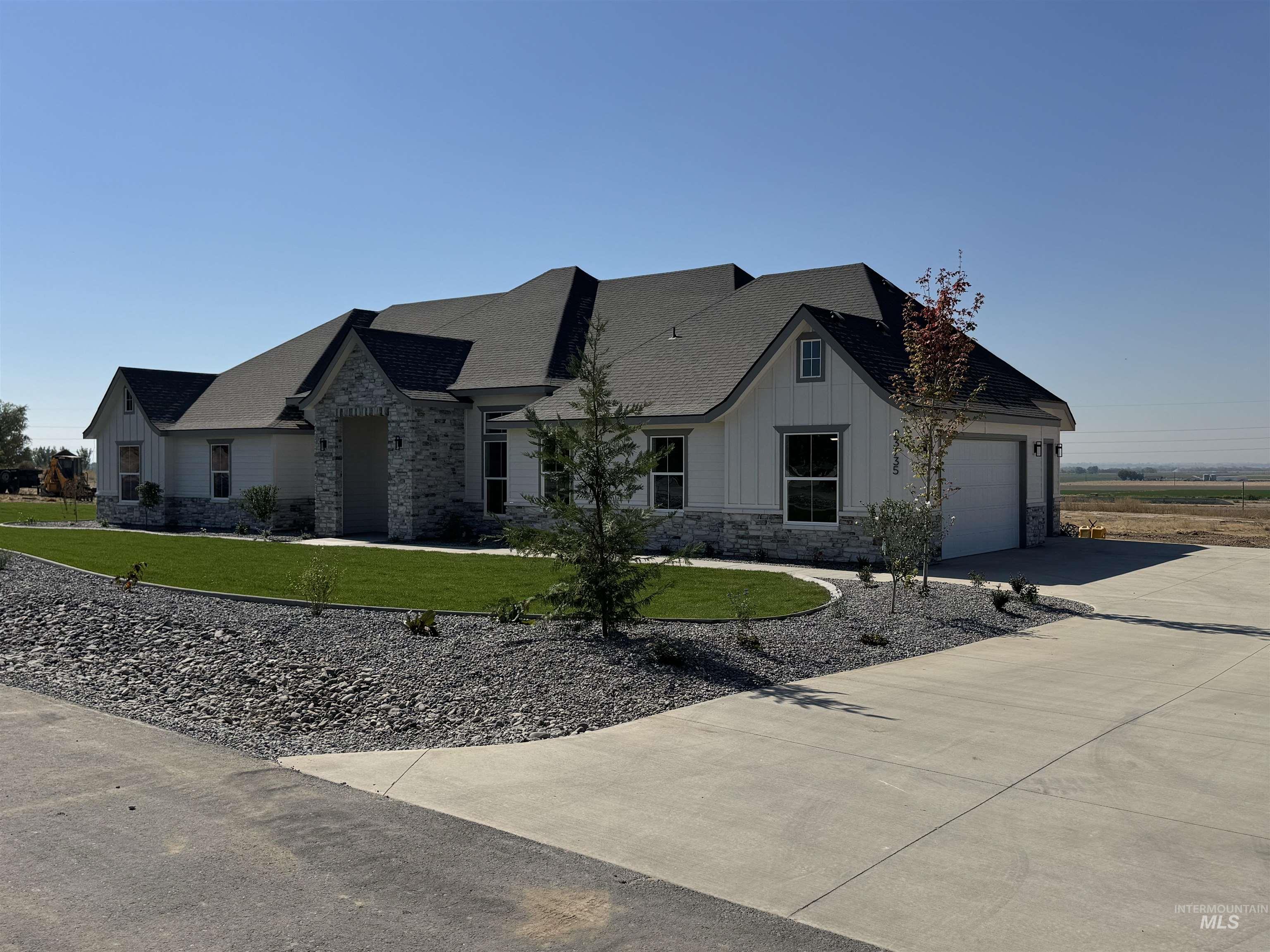 View of front of property with board and batten siding, stone siding, driveway, and a front lawn