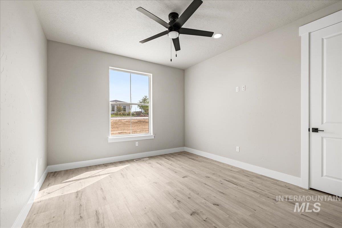 Empty room featuring a textured ceiling, light wood-type flooring, and ceiling fan
