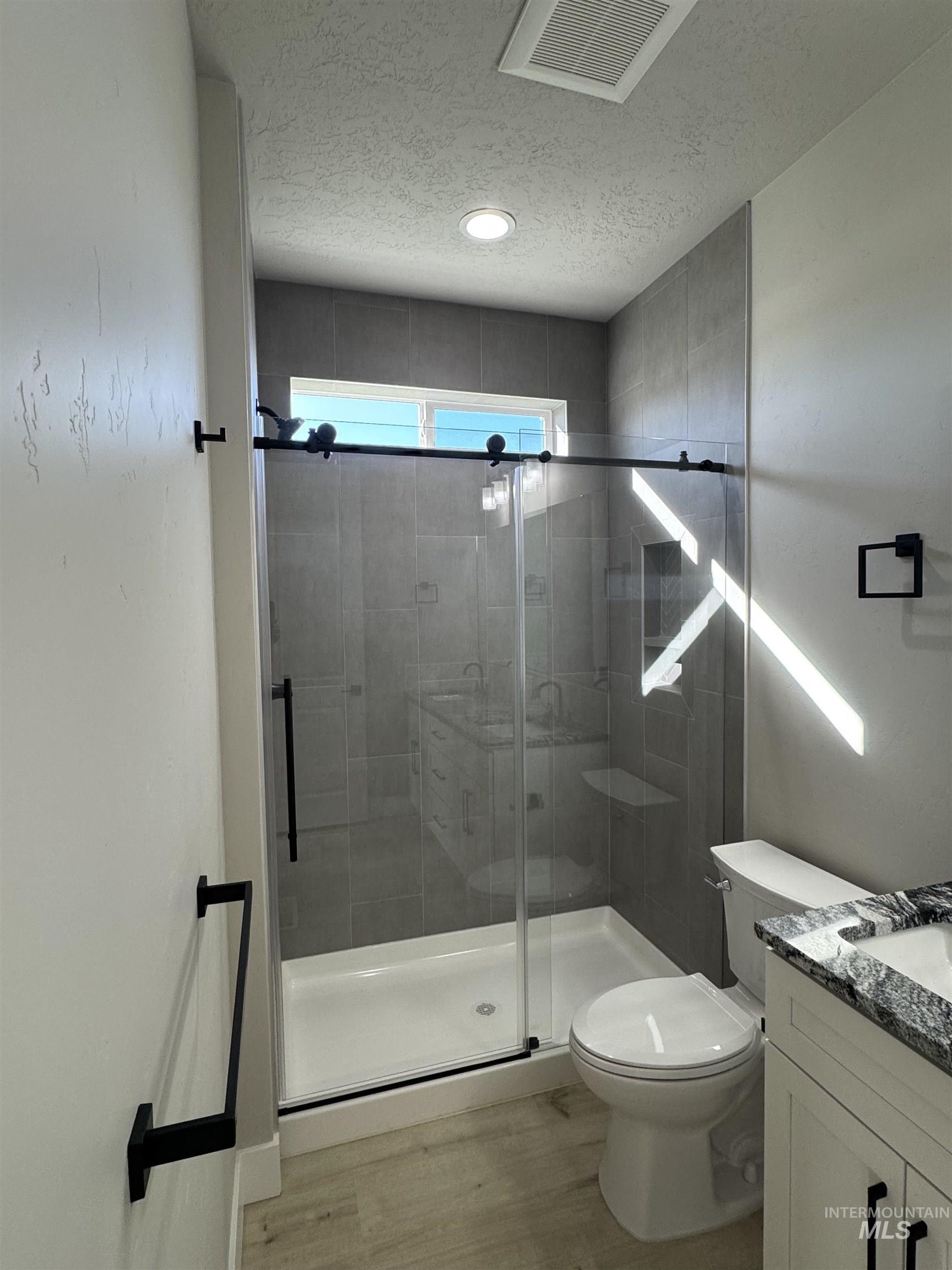 Full bathroom featuring vanity, a textured ceiling, a shower stall, and light wood finished floors