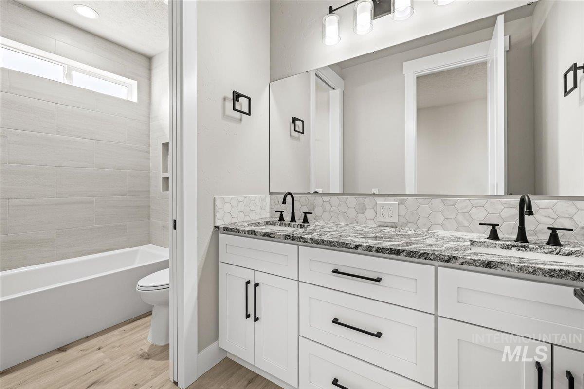 Full bath featuring light wood-style flooring, double vanity, tasteful backsplash, bathing tub / shower combination, and a textured ceiling