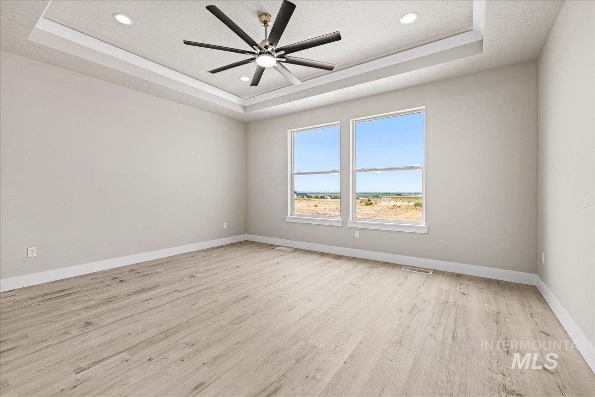 Spare room with a tray ceiling, light wood-style floors, a ceiling fan, and recessed lighting