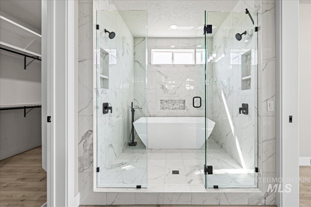 Full bath with a spacious closet, a marble finish shower, a freestanding bath, and a textured ceiling