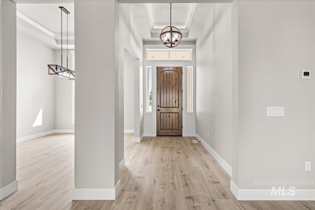 Foyer with a chandelier, a raised ceiling, and light wood-style floors