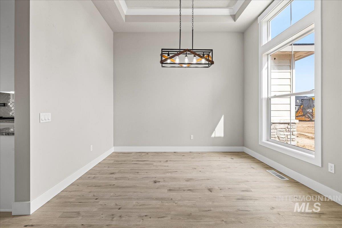 Unfurnished dining area featuring a raised ceiling, light wood-style floors, and a chandelier