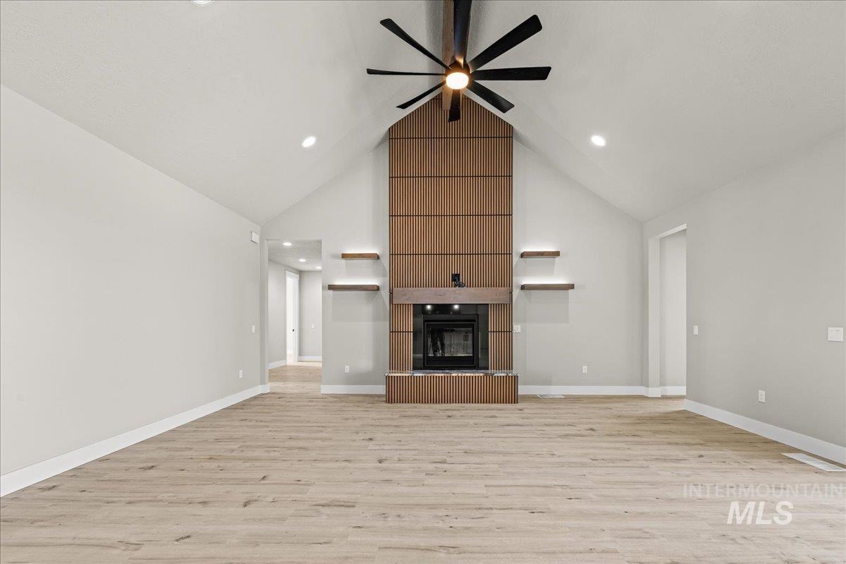 Unfurnished living room featuring a fireplace, light wood-style floors, high vaulted ceiling, a ceiling fan, and recessed lighting