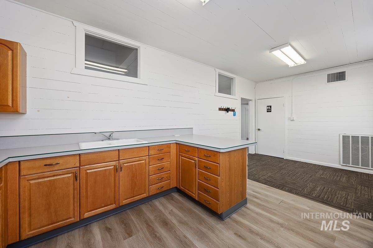 Kitchen featuring a peninsula, brown cabinets, light countertops, light wood-style flooring, and wood walls