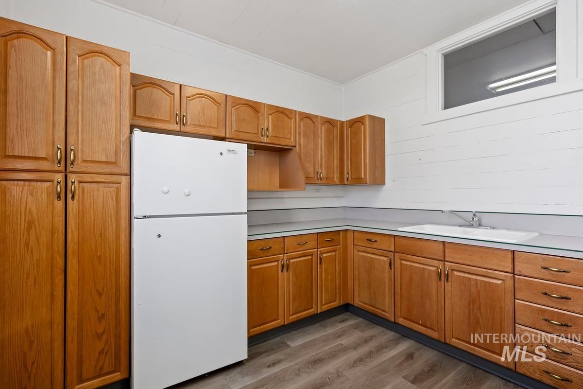 Kitchen featuring freestanding refrigerator, dark wood-type flooring, light countertops, and brown cabinets
