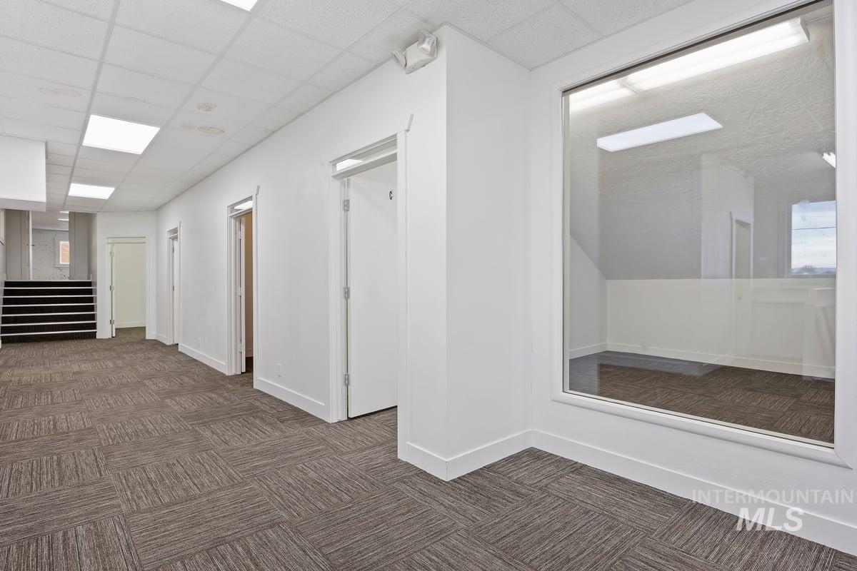 Hall with dark carpet, a drop ceiling, and stairs