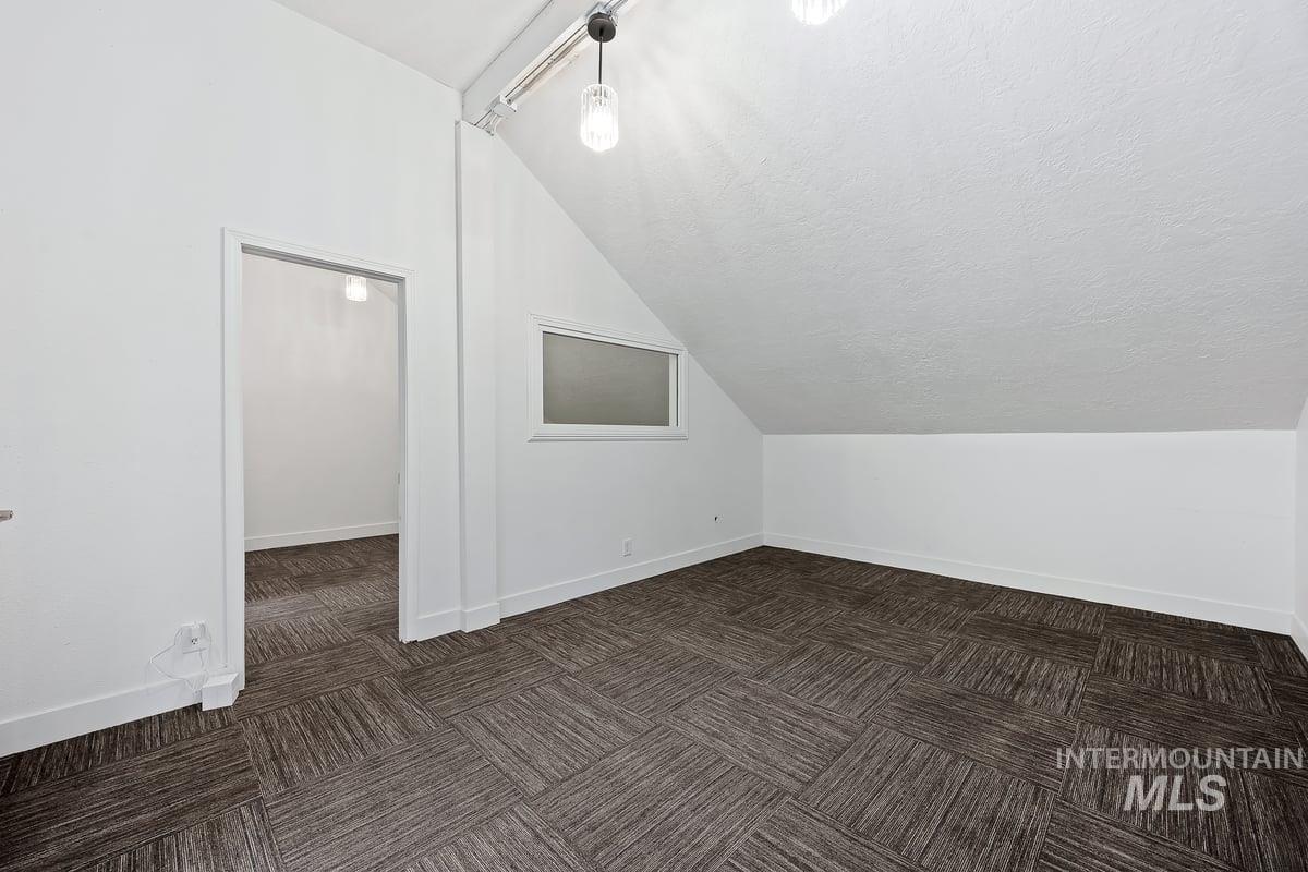 Bonus room with vaulted ceiling, dark colored carpet, and a textured ceiling