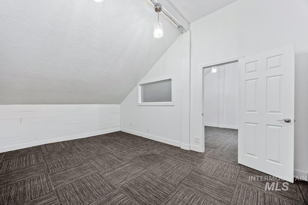 Additional living space with a textured ceiling, dark colored carpet, and lofted ceiling