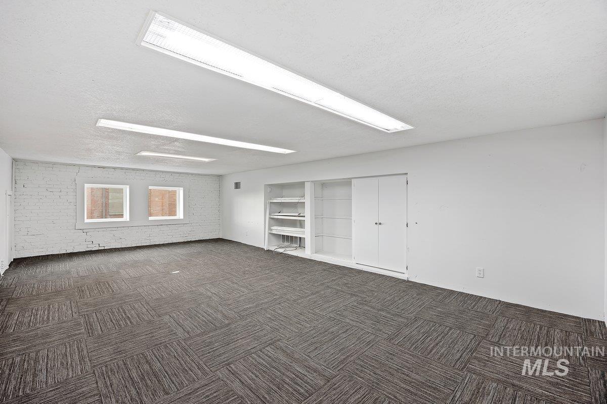 Spare room featuring a textured ceiling, dark carpet, and brick wall