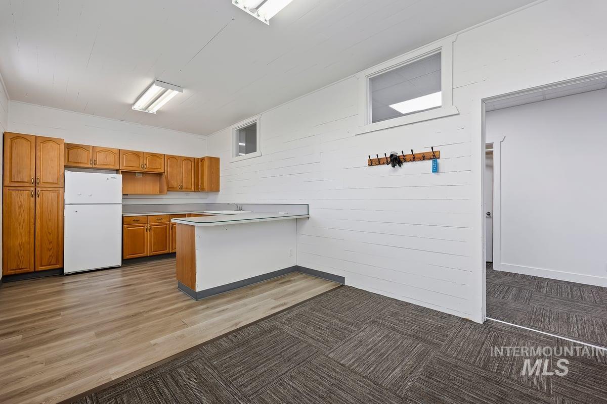 Kitchen featuring freestanding refrigerator, light countertops, brown cabinetry, a peninsula, and wooden walls
