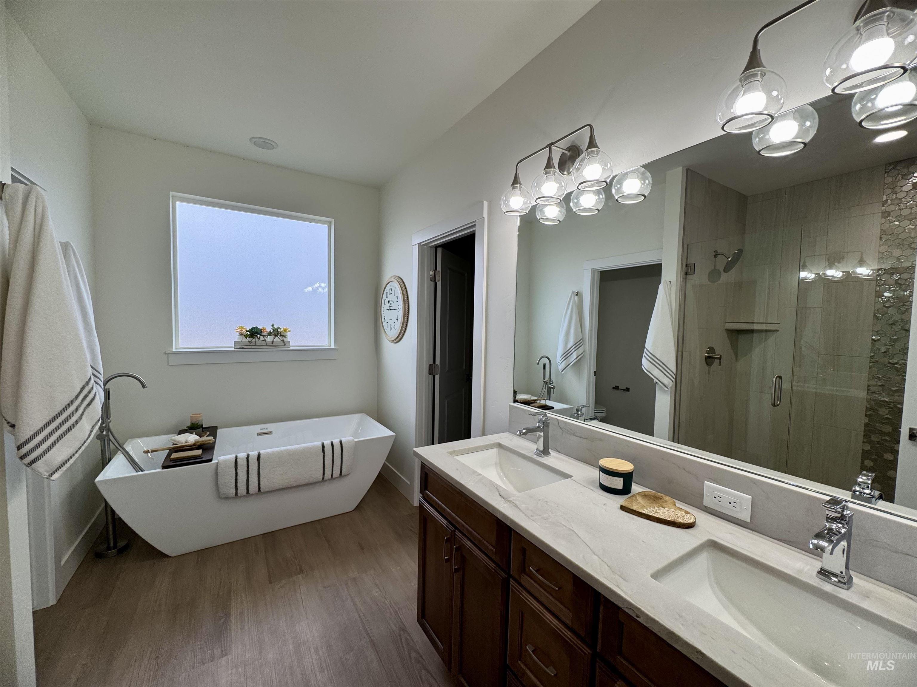 Full bathroom featuring a freestanding tub, double vanity, dark wood finished floors, and a stall shower