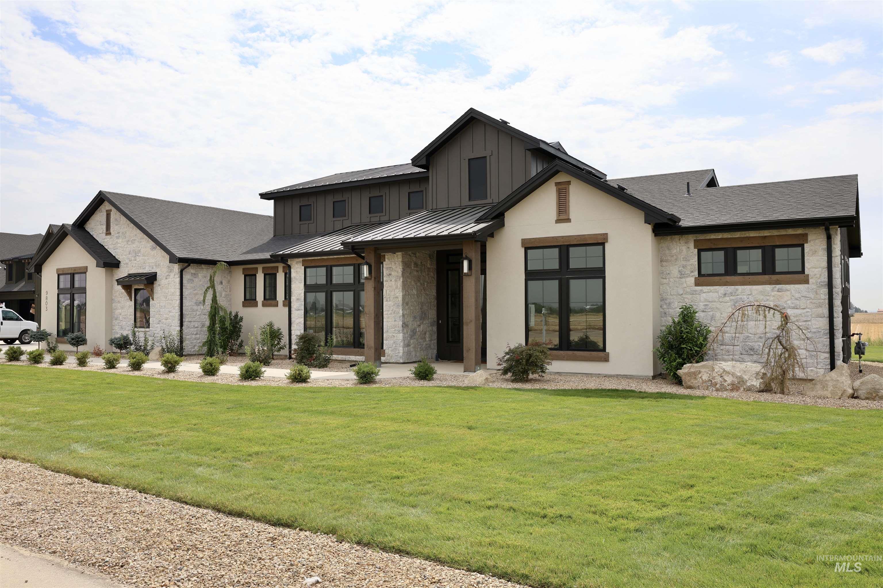 Modern farmhouse style home featuring stone siding, a standing seam roof, a front yard, a metal roof, and a shingled roof
