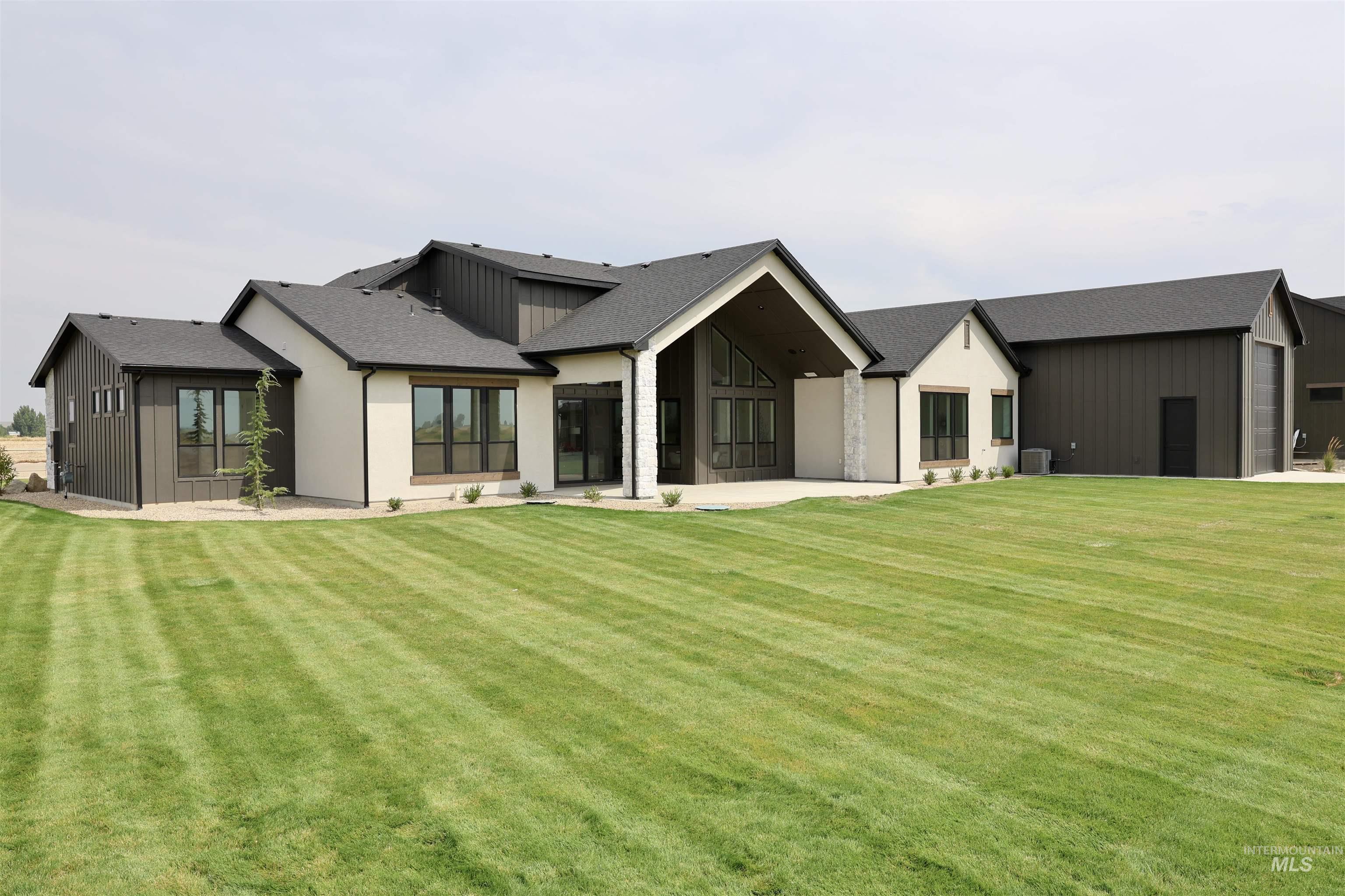 Rear view of house featuring a patio area, a lawn, a shingled roof, and board and batten siding