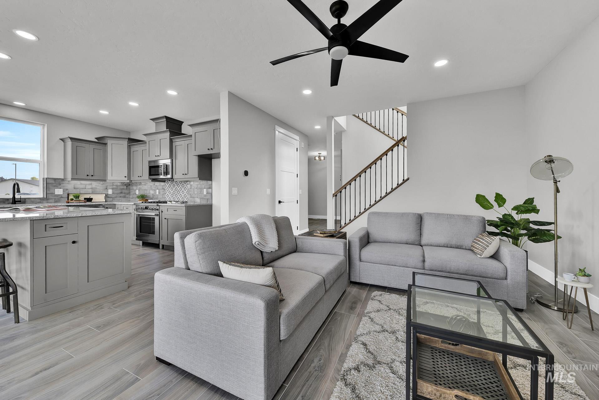 Living room featuring light wood finished floors, a ceiling fan, recessed lighting, and stairway