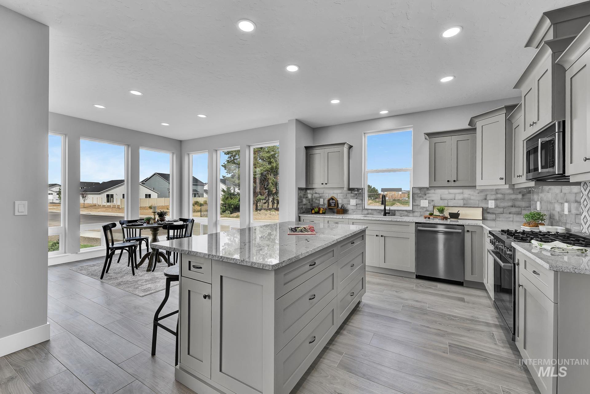 Kitchen featuring appliances with stainless steel finishes, gray cabinetry, backsplash, light stone counters, and a kitchen breakfast bar