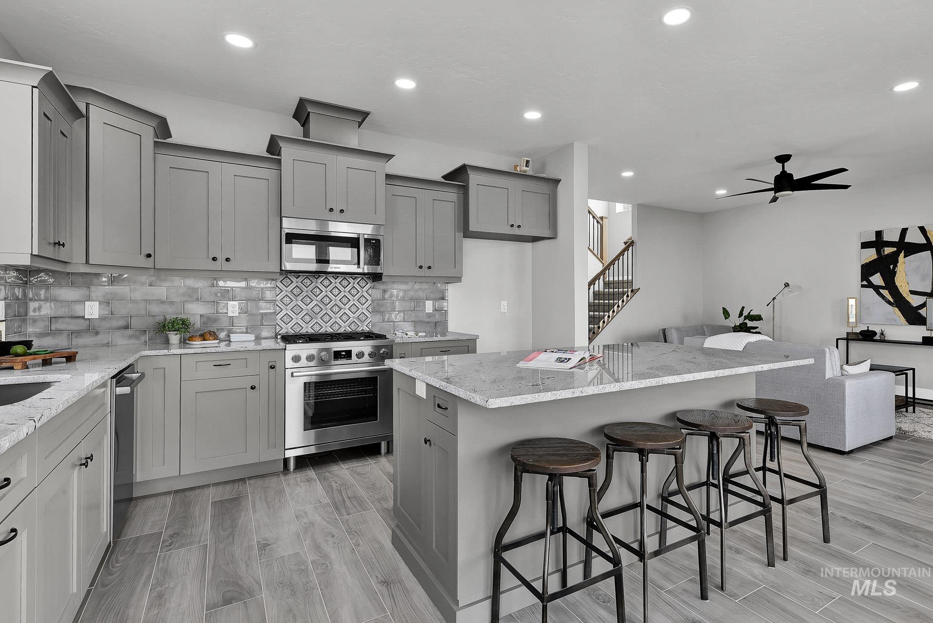 Kitchen with gray cabinets, a breakfast bar area, light stone countertops, backsplash, and a center island