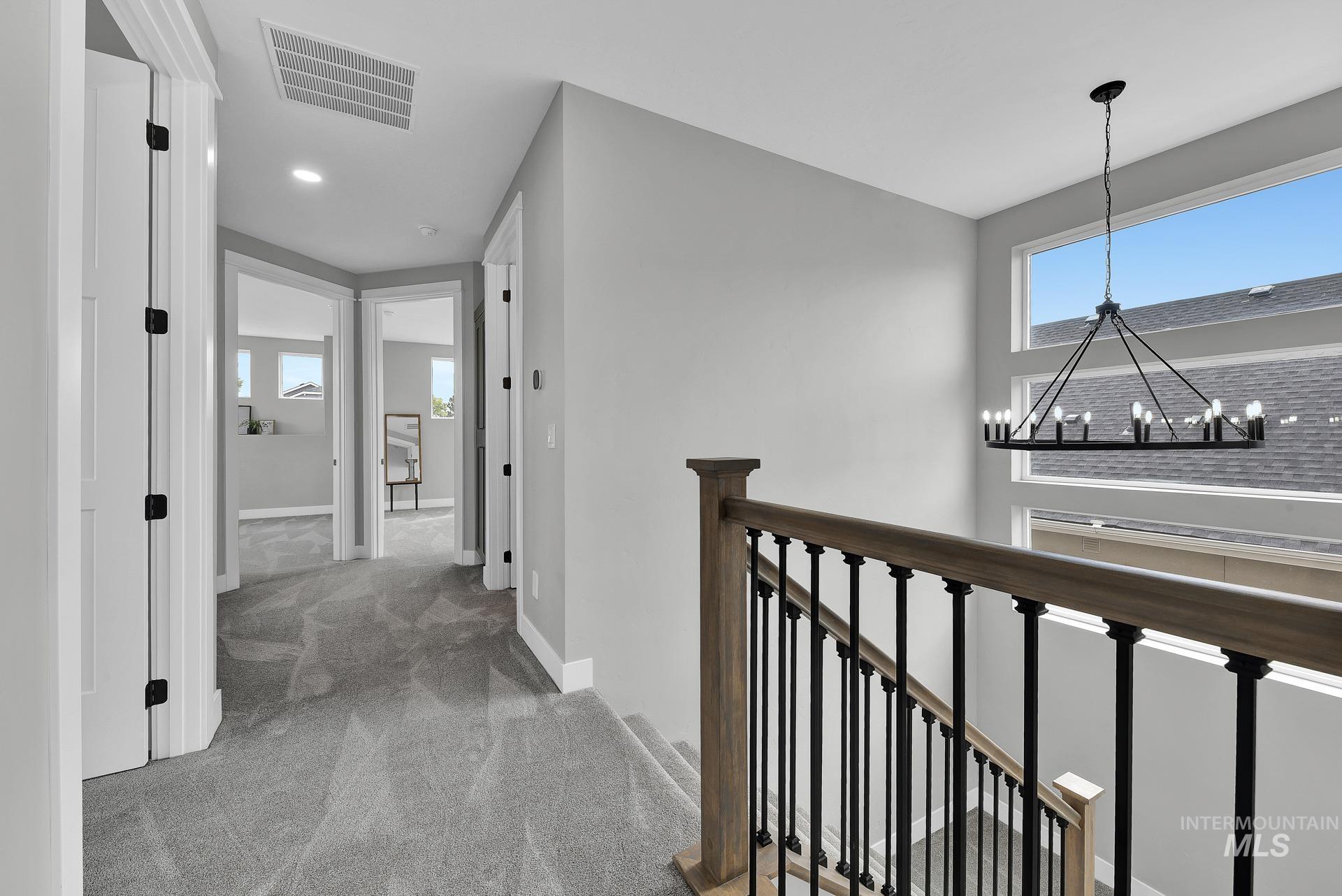 Corridor featuring light colored carpet, an upstairs landing, and a chandelier
