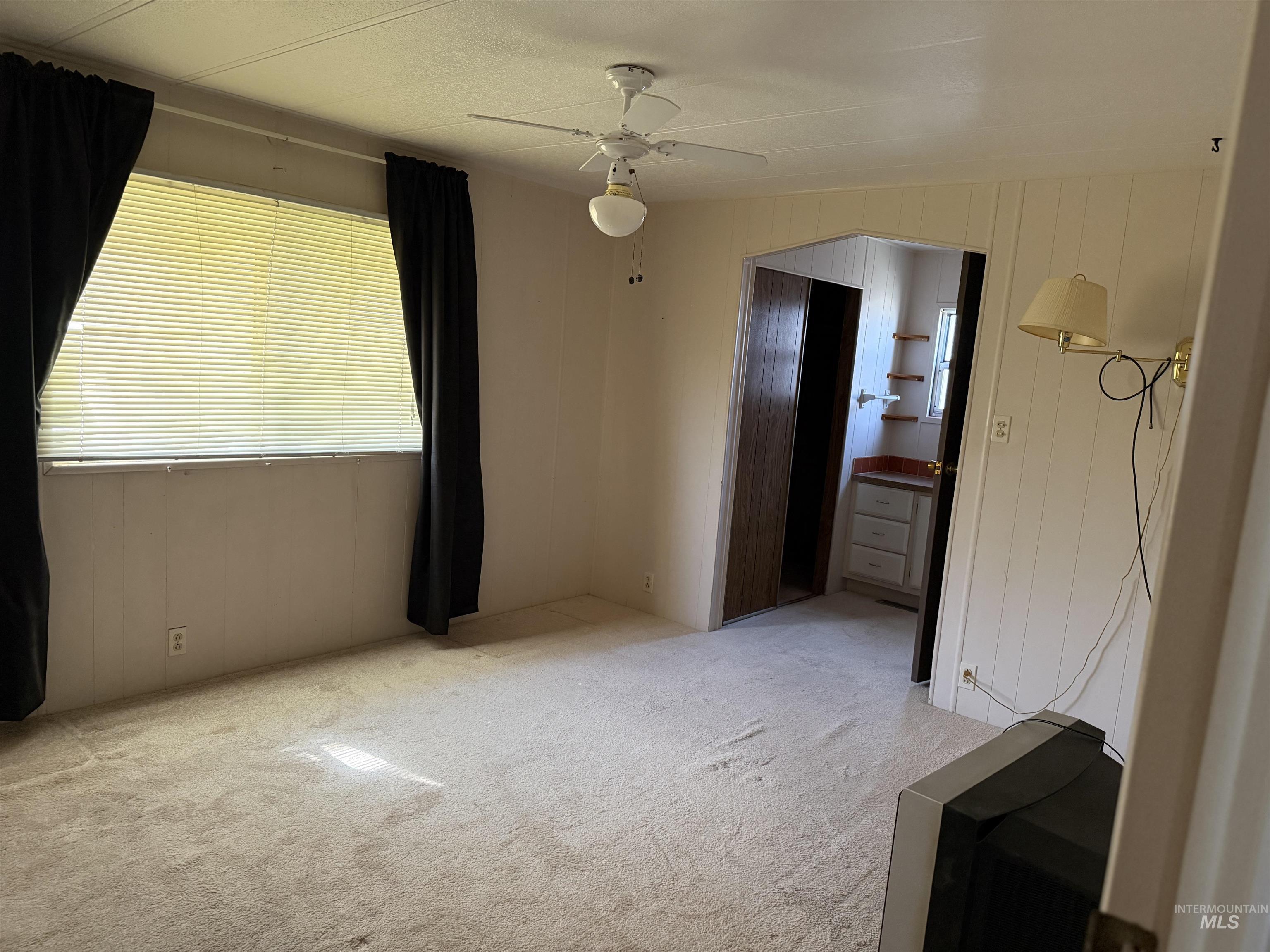 Unfurnished bedroom featuring light colored carpet, wood walls, and a ceiling fan