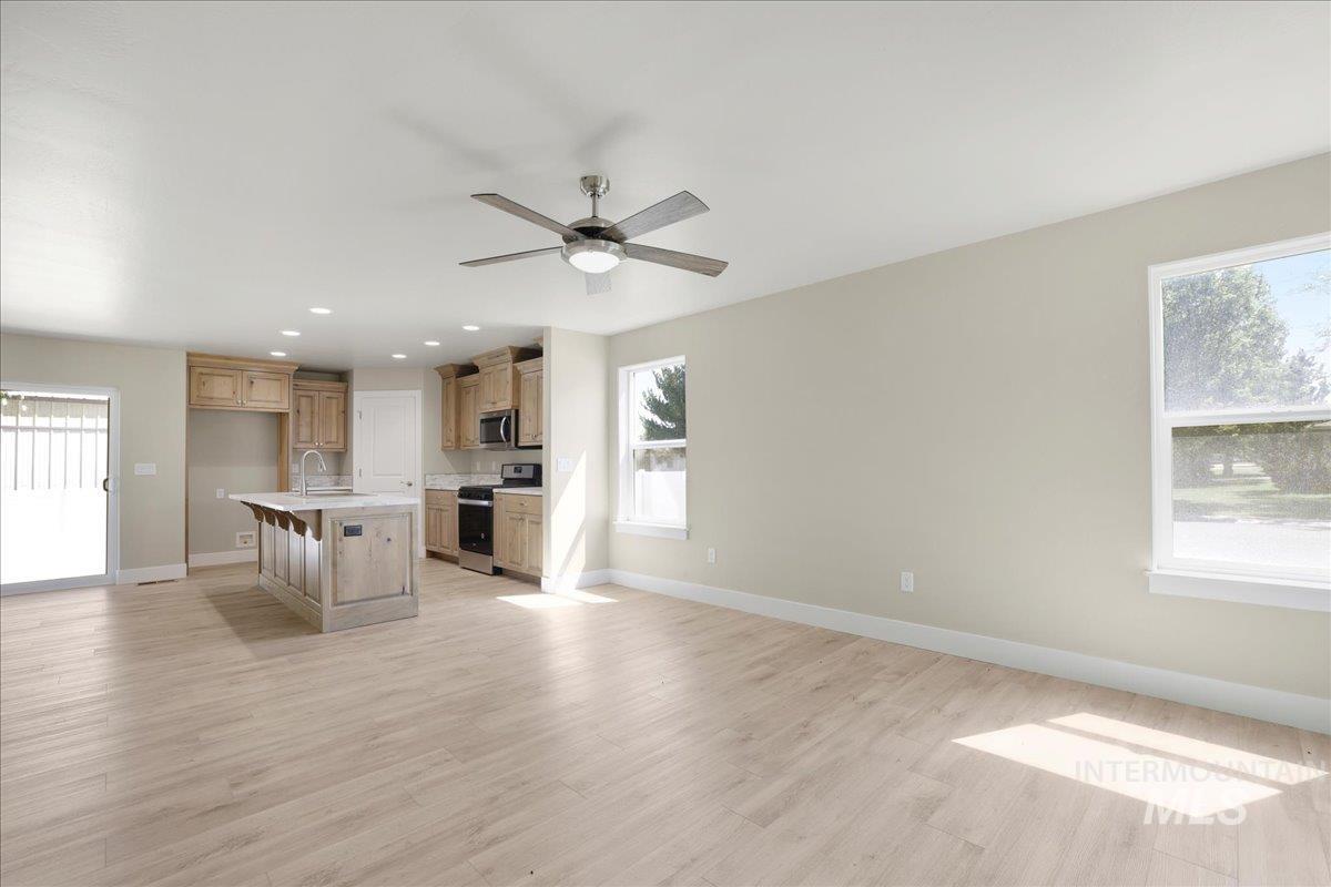 Unfurnished living room with healthy amount of natural light, light wood-style flooring, ceiling fan, and recessed lighting
