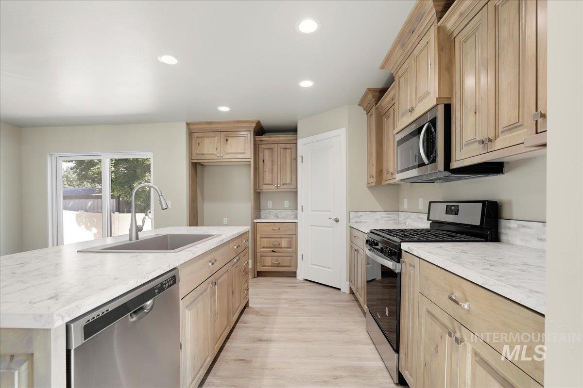 Kitchen featuring appliances with stainless steel finishes, light brown cabinets, light wood-style floors, a kitchen island with sink, and recessed lighting