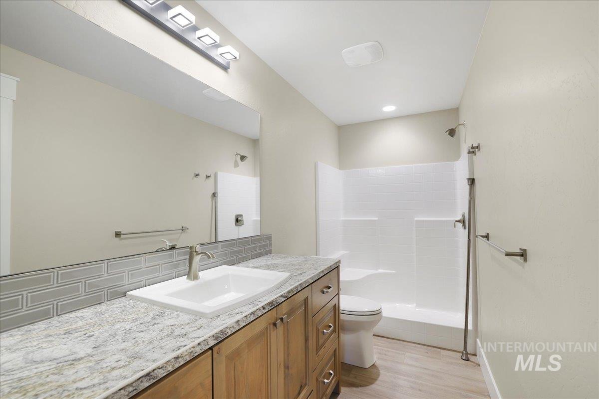 Full bathroom with tiled shower, vanity, backsplash, and wood finished floors