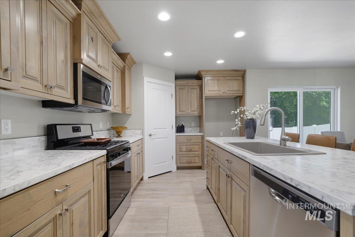 Kitchen with appliances with stainless steel finishes, light wood finished floors, recessed lighting, light stone countertops, and light brown cabinetry