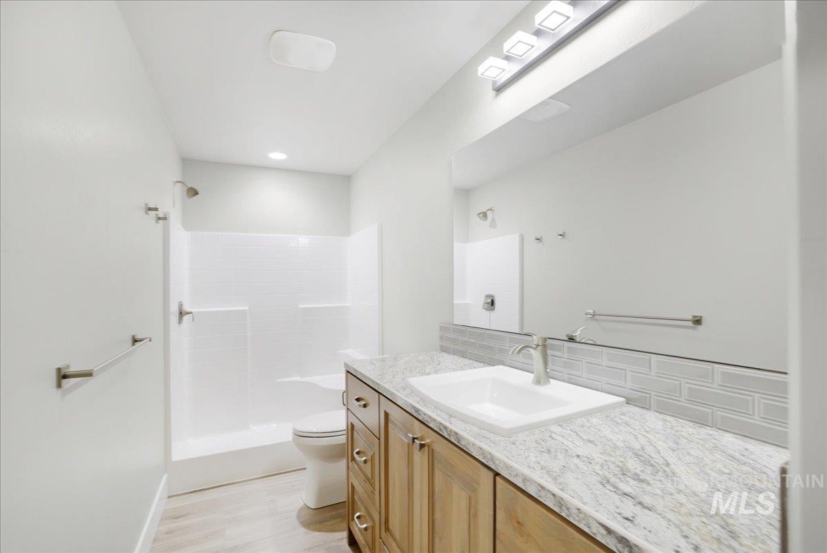 Full bath featuring a tile shower, tasteful backsplash, vanity, and wood finished floors