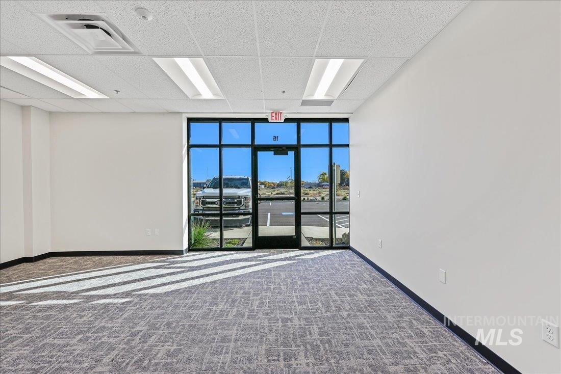 Unfurnished room featuring a wall of windows, a drop ceiling, carpet flooring, and a smoke detector