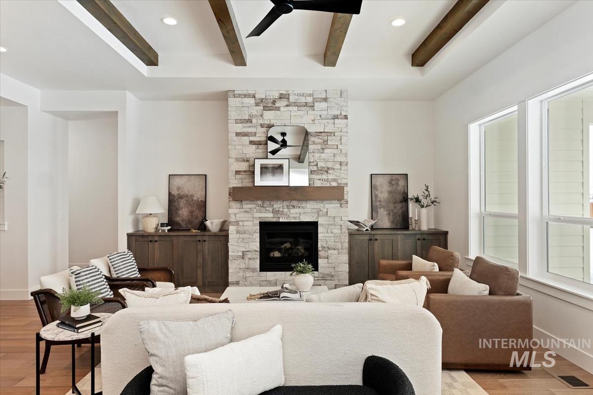 Living area with a ceiling fan, light wood-type flooring, beamed ceiling, a stone fireplace, and recessed lighting