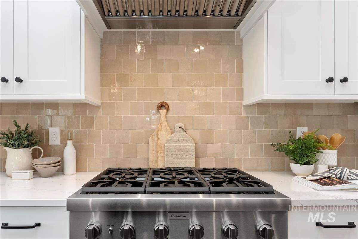Kitchen featuring ventilation hood, white cabinetry, decorative backsplash, and light stone countertops