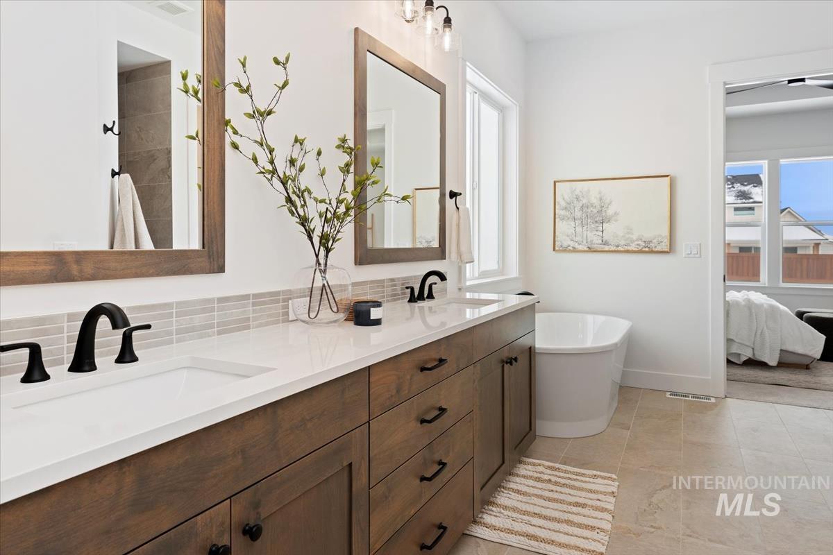 Ensuite bathroom featuring double vanity, a freestanding bath, and decorative backsplash