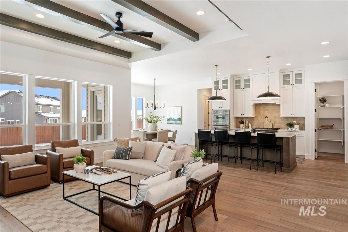 Living area featuring light wood-style floors, a ceiling fan, a chandelier, recessed lighting, and beam ceiling