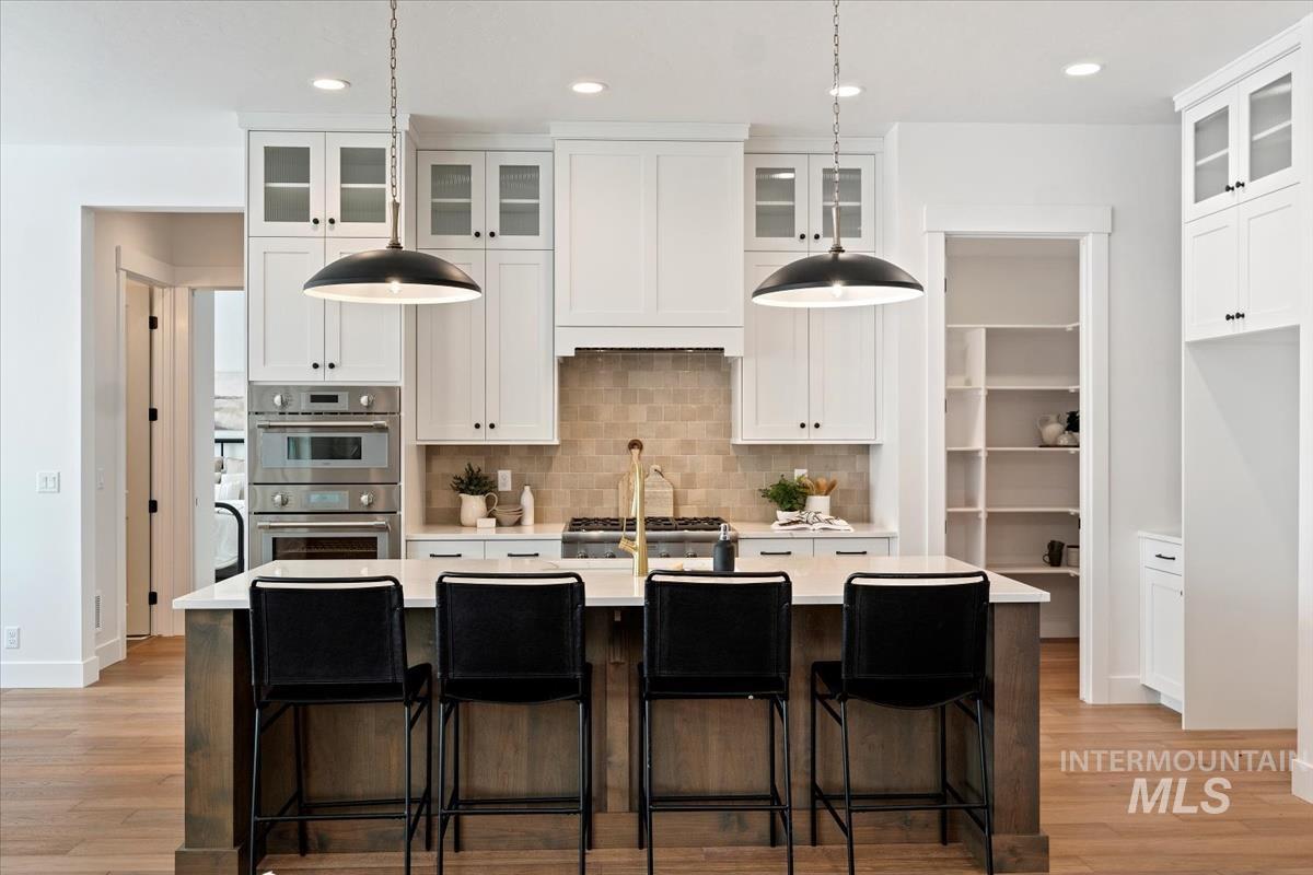 Kitchen featuring double oven, light countertops, light wood-style flooring, backsplash, and recessed lighting