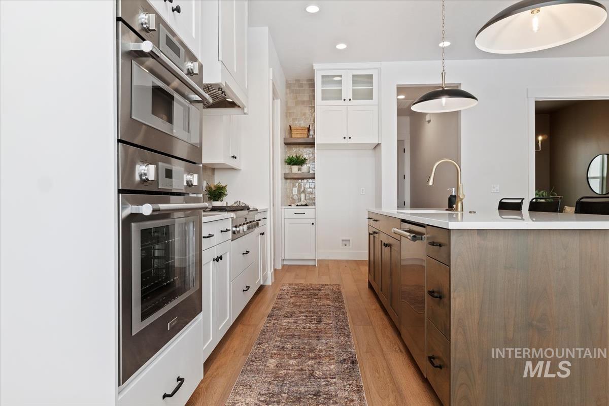 Kitchen with stainless steel appliances, a kitchen island with sink, light wood-style flooring, white cabinets, and pendant lighting