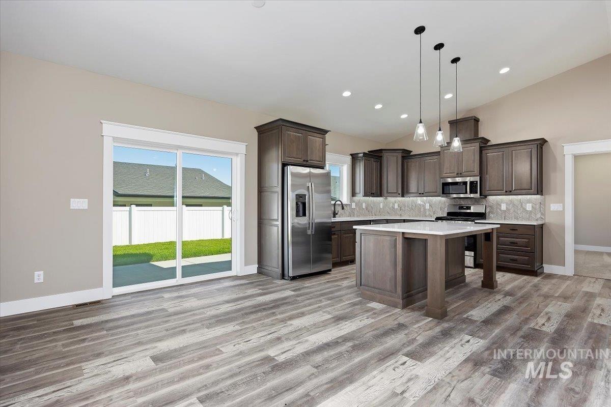 Kitchen featuring decorative backsplash, appliances with stainless steel finishes, dark brown cabinets, hanging light fixtures, and a breakfast bar