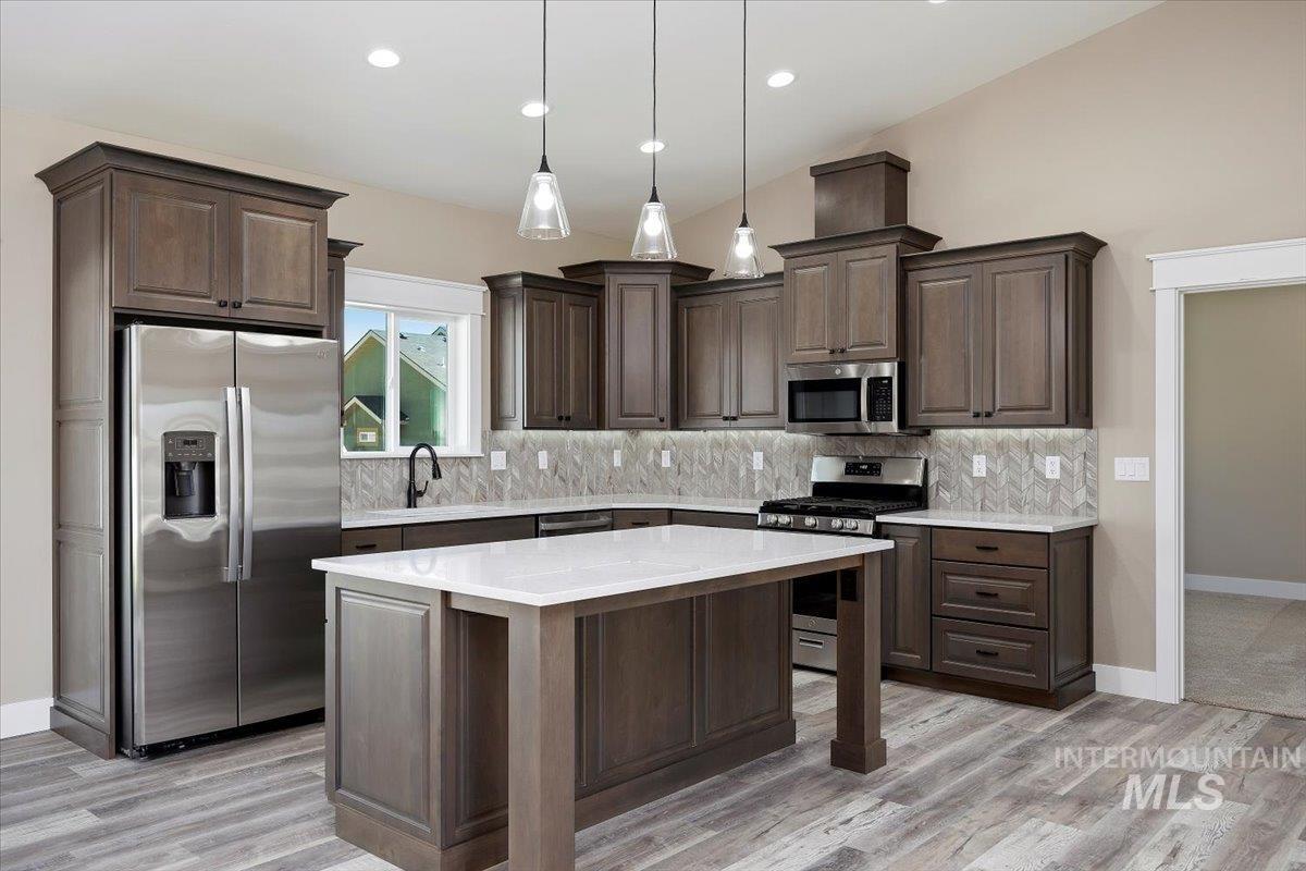 Kitchen featuring stainless steel appliances, dark brown cabinets, decorative light fixtures, a kitchen island, and recessed lighting