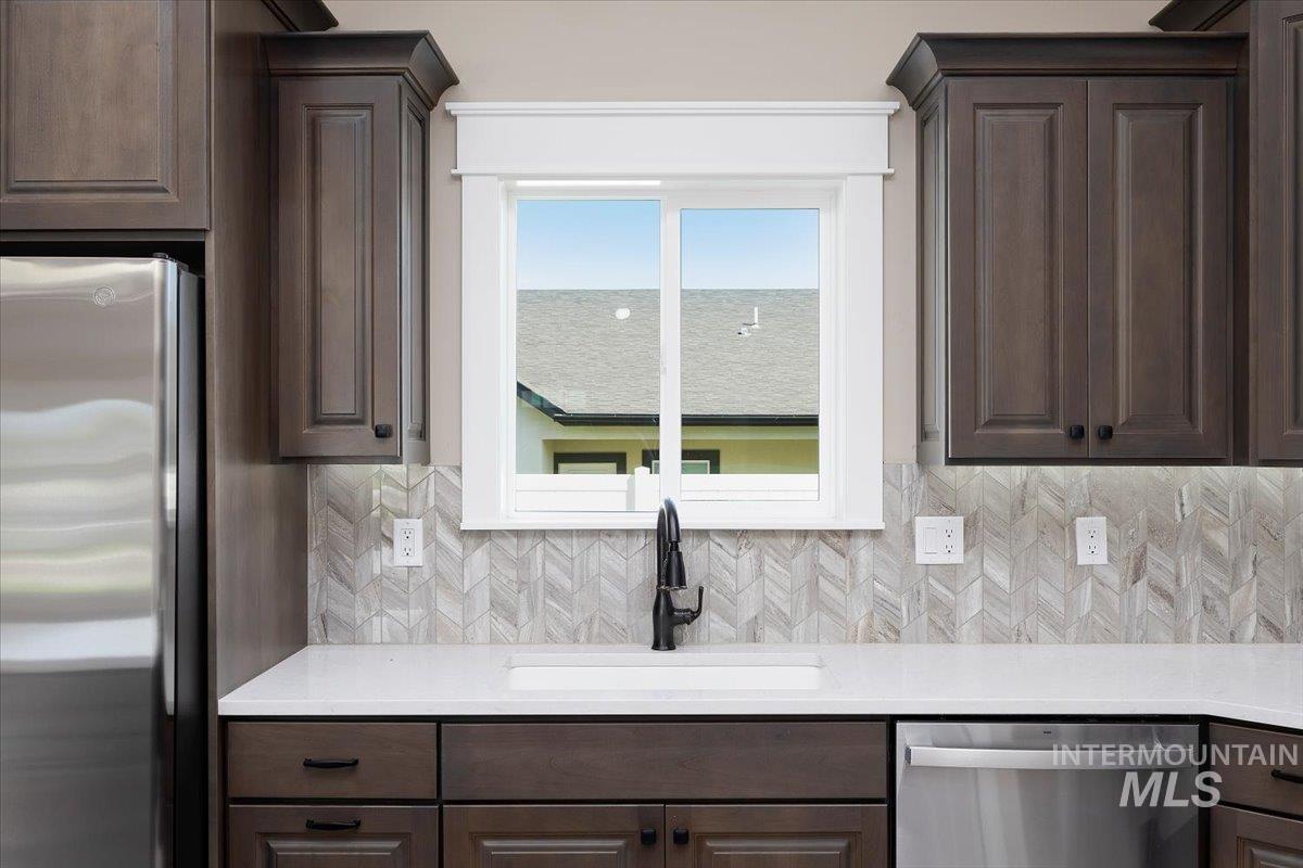 Kitchen featuring dark brown cabinets, stainless steel appliances, tasteful backsplash, and light stone counters