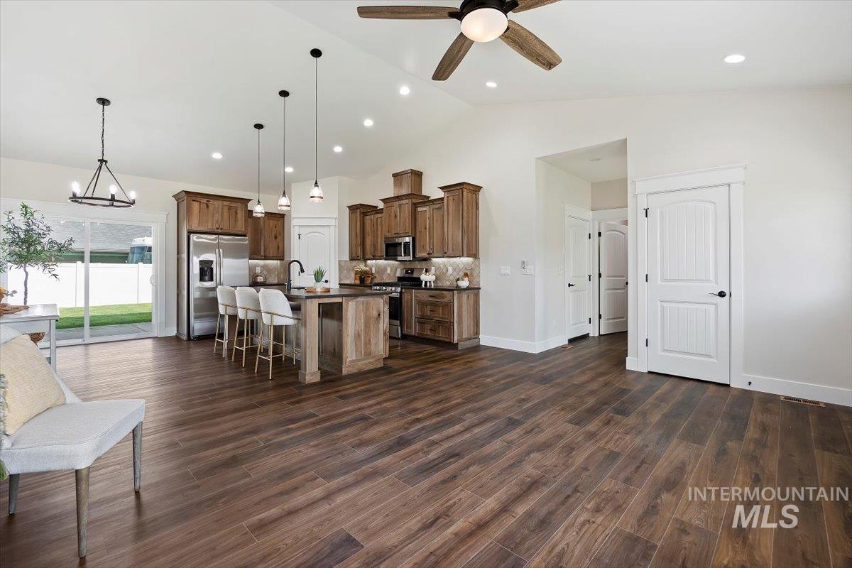 Kitchen featuring decorative light fixtures, a kitchen bar, appliances with stainless steel finishes, an island with sink, and backsplash