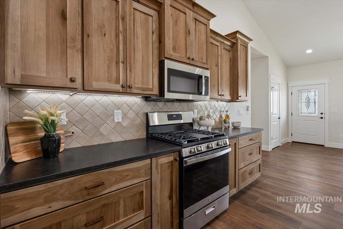 Kitchen featuring stainless steel appliances, decorative backsplash, dark wood-type flooring, brown cabinetry, and recessed lighting