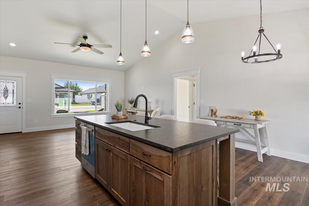 Kitchen featuring a kitchen island with sink, vaulted ceiling, dark wood-style flooring, hanging light fixtures, and a ceiling fan