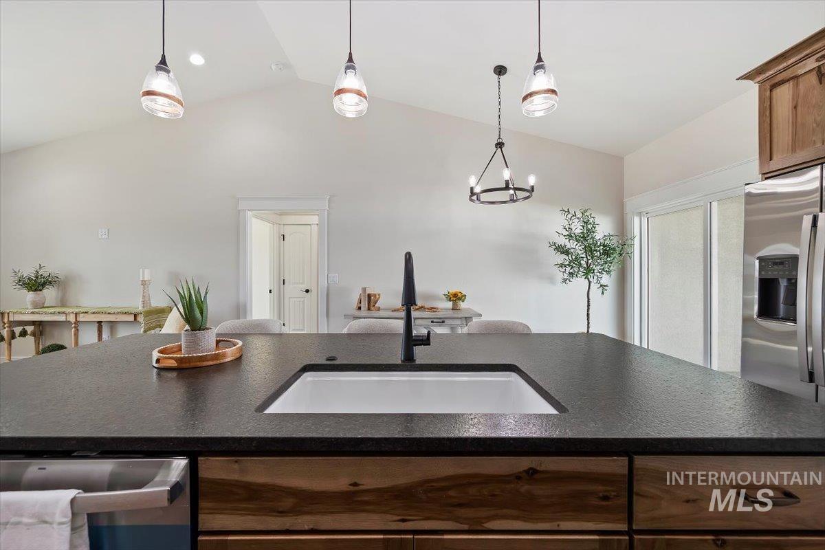 Kitchen featuring lofted ceiling, decorative light fixtures, appliances with stainless steel finishes, dark stone countertops, and a chandelier